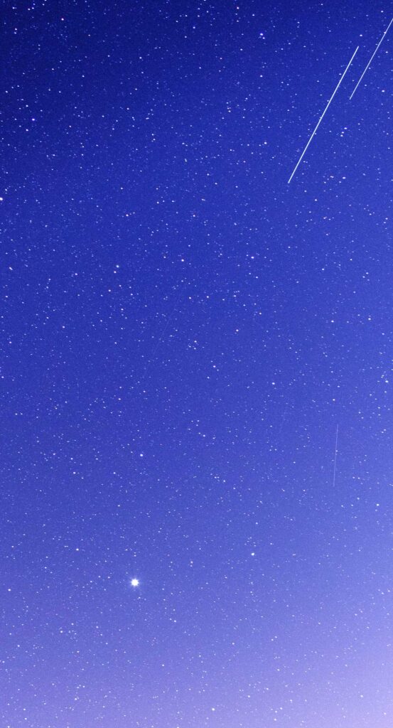 Free phone wallpaper image of a blue and purple night sky with stars, a planet, and a shooting star.