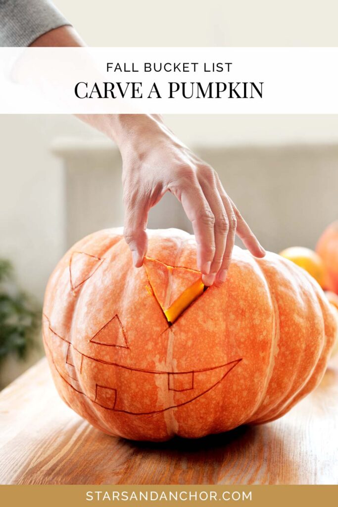A pumpkin with a jack-o-lantern face drawn on it and someone's hand removing the eye of the jack-o-lantern, with text that says, "fall bucket list: carve a pumpkin."