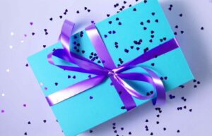 A gift wrapped in turquoise paper with purple ribbon and heart confetti.