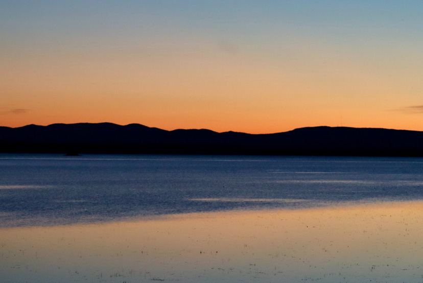 Lake Champlain at sunset with mountains silhouetted in the distance.