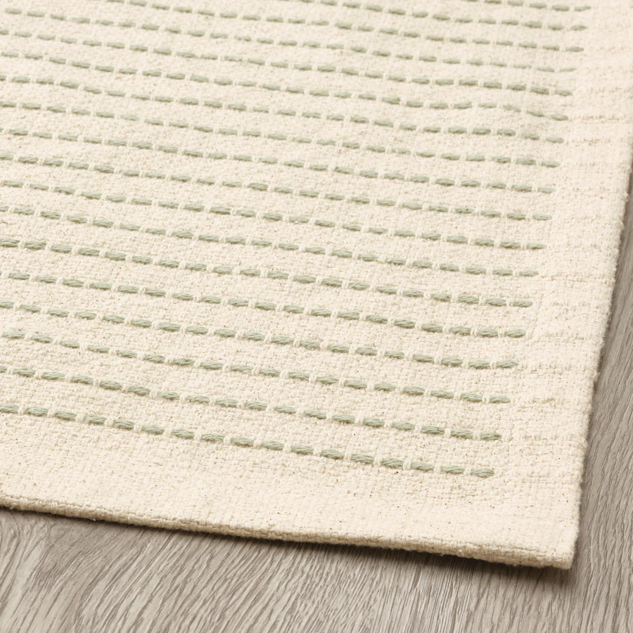 Detail of an off-white rug with light green stitching.