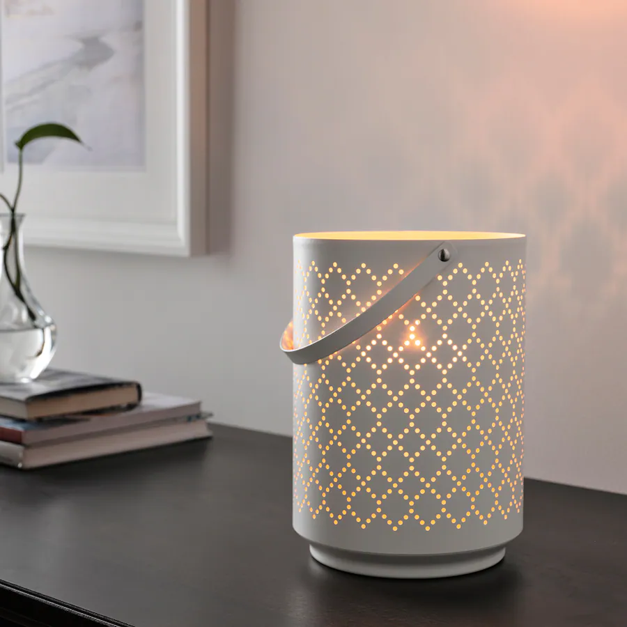 A white lantern on a dresser with holes in a diamond pattern, and a candle lit inside.