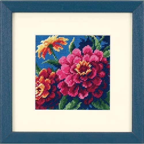 A framed needlepoint project of colorful zinnias on a blue background.