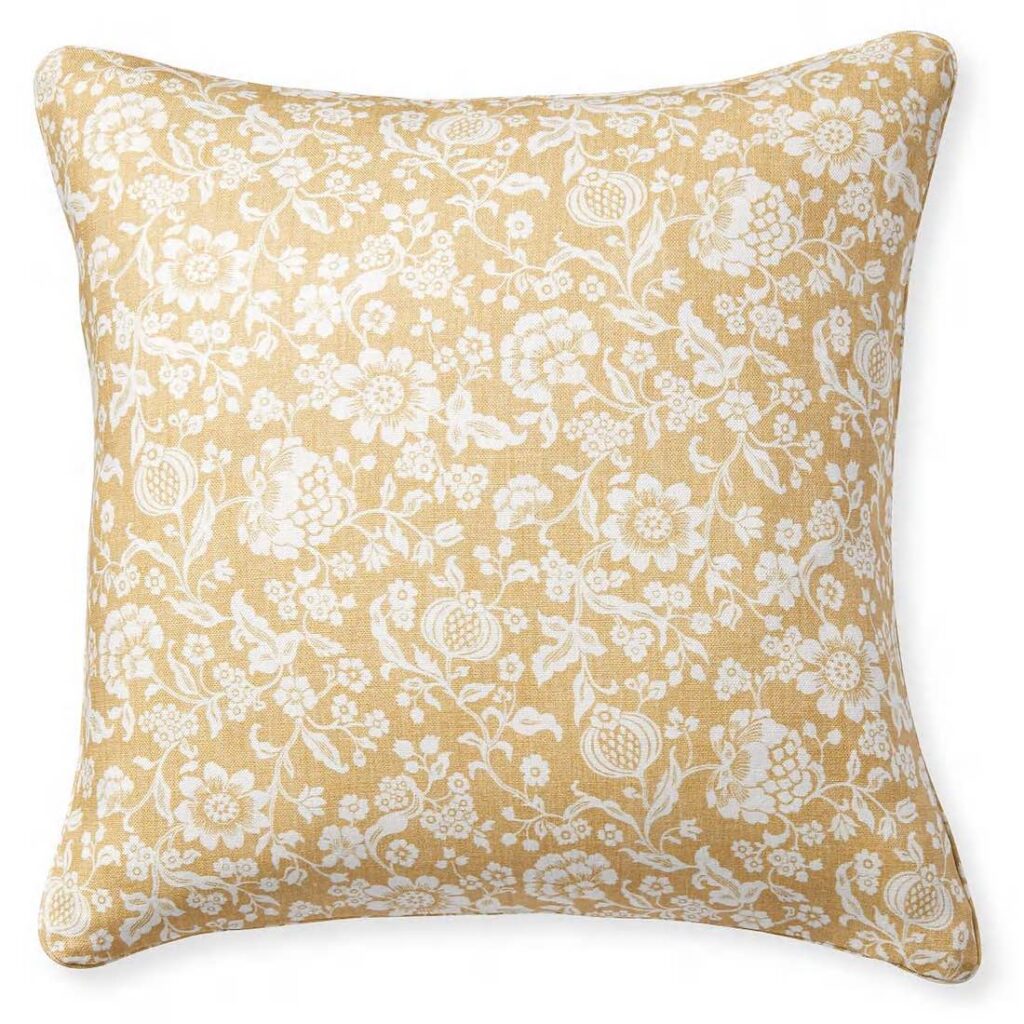 A neutral/golden throw pillow with a white floral pattern all over.