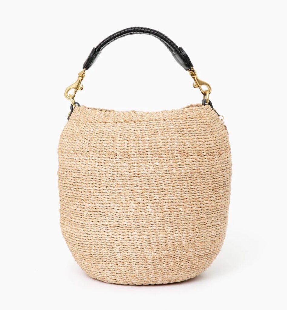 A woven straw tote bag with a black strap and gold hardware.