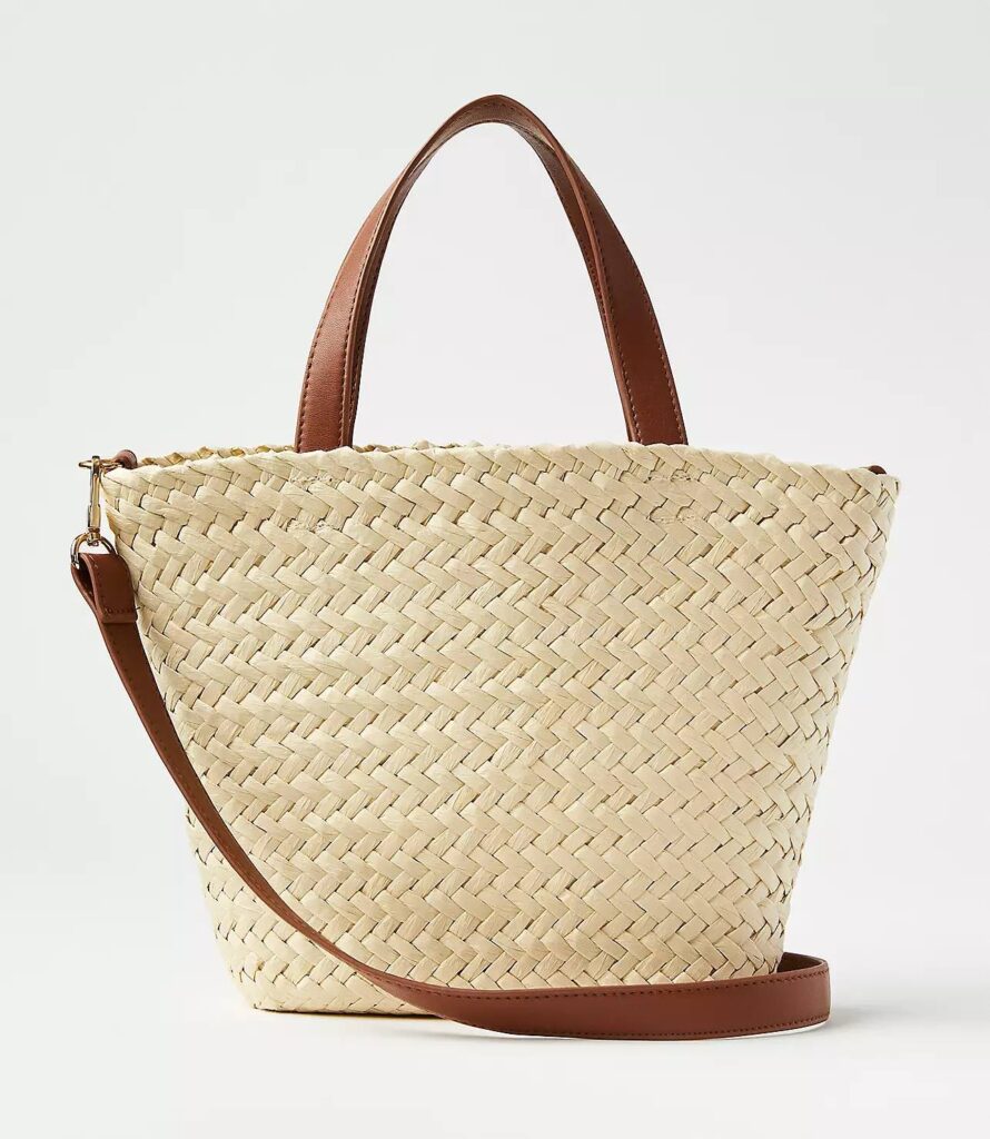 A woven straw tote bag with brown handles and a brown crossbody strap.