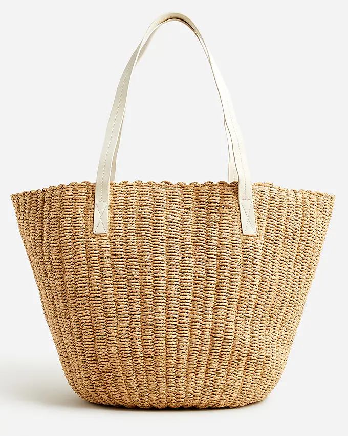 A woven straw tote bag with off-white handles.