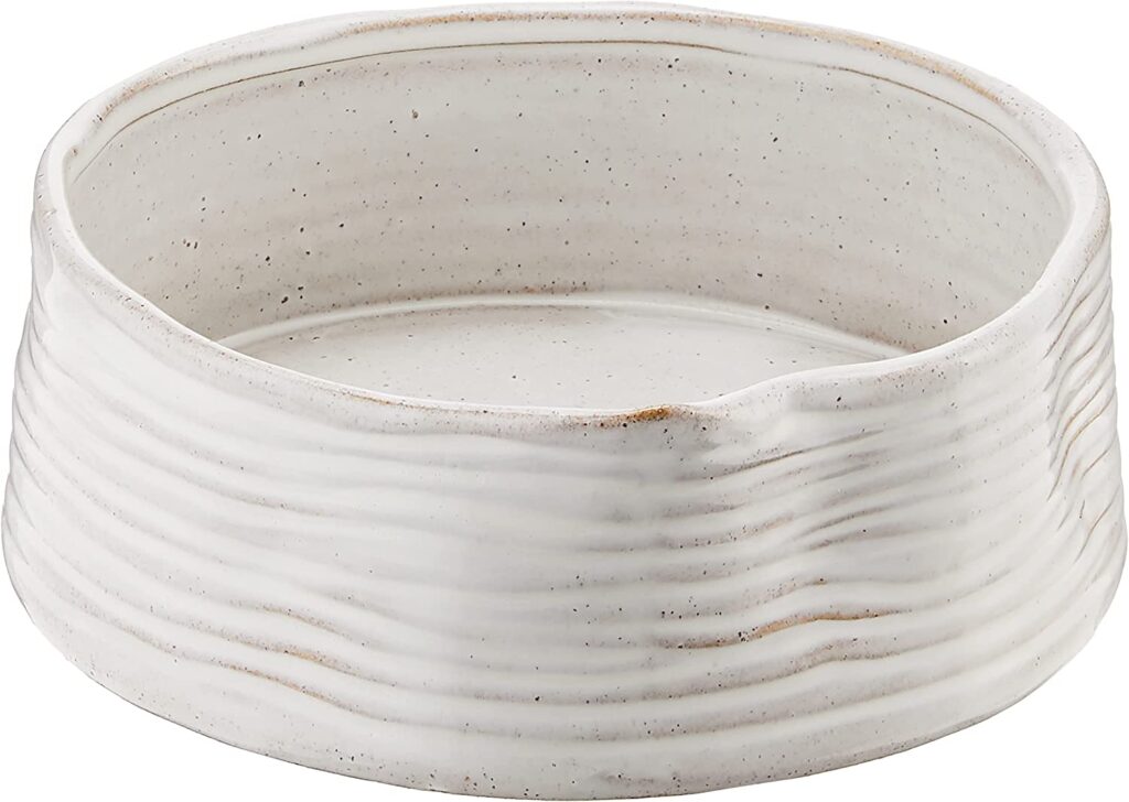 A clay and white glazed stoneware bowl with a wavy ribbed texture and organic round shape.