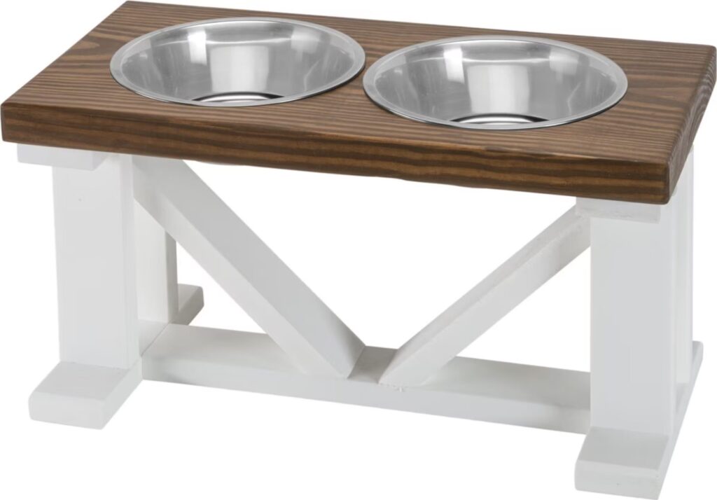 Two stainless steel dog bowls on a white wood elevated stand with a brown wood top.