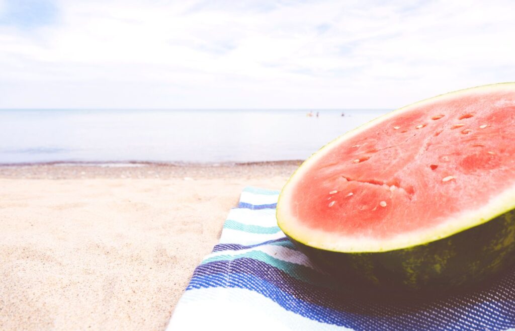 Half of a watermelon on a beach blanket at the beach.