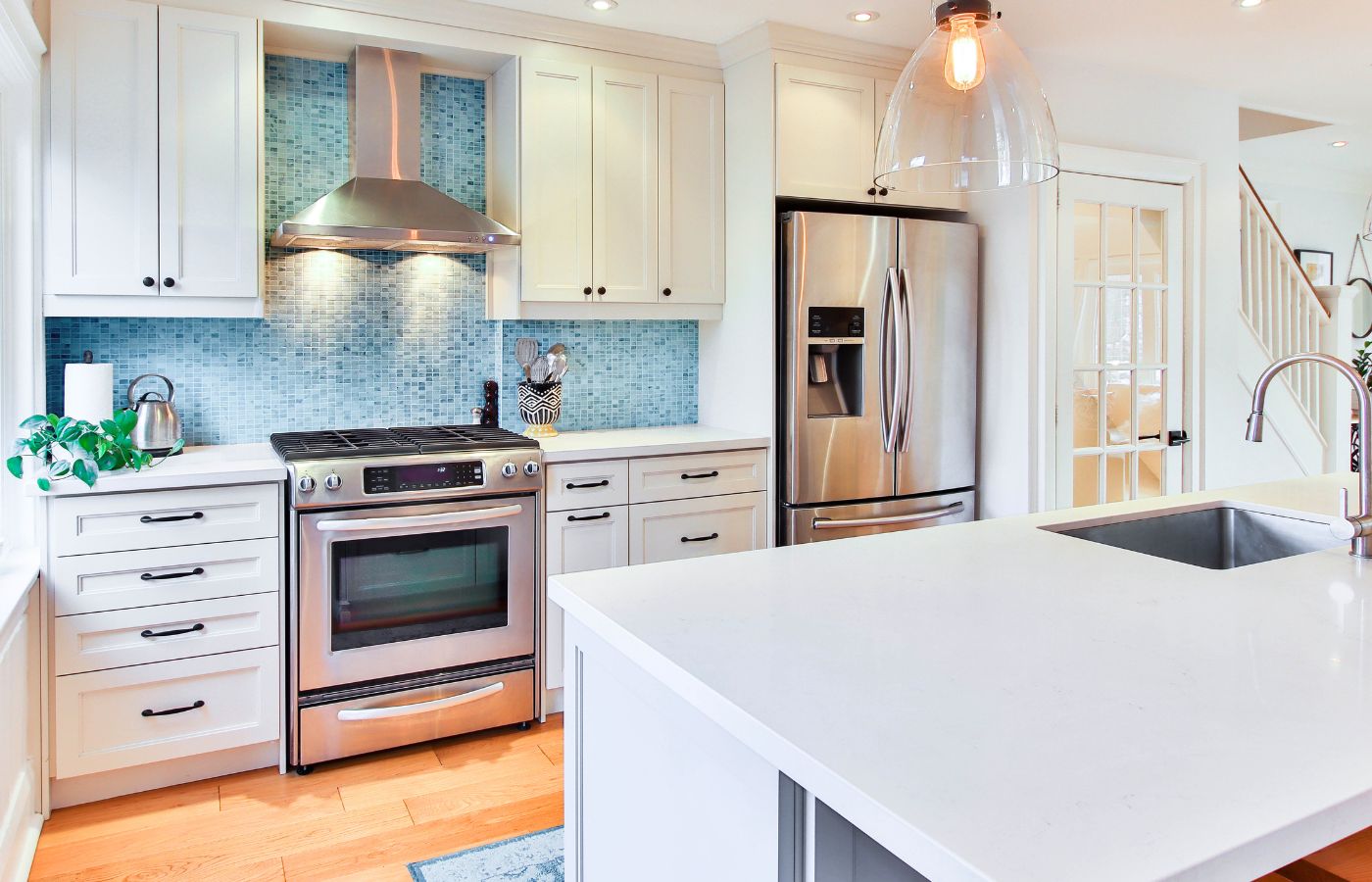 A clean kitchen with white countertops and cabinets and a blue tile backsplash.