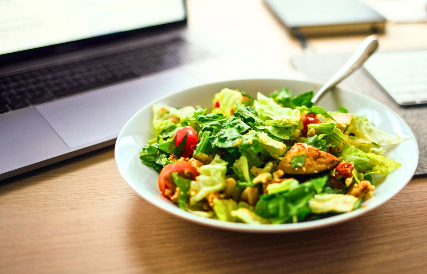 An example of one of the gluten free lunch ideas for work, a salad with fresh and roasted vegetables on a desk in front of a laptop.