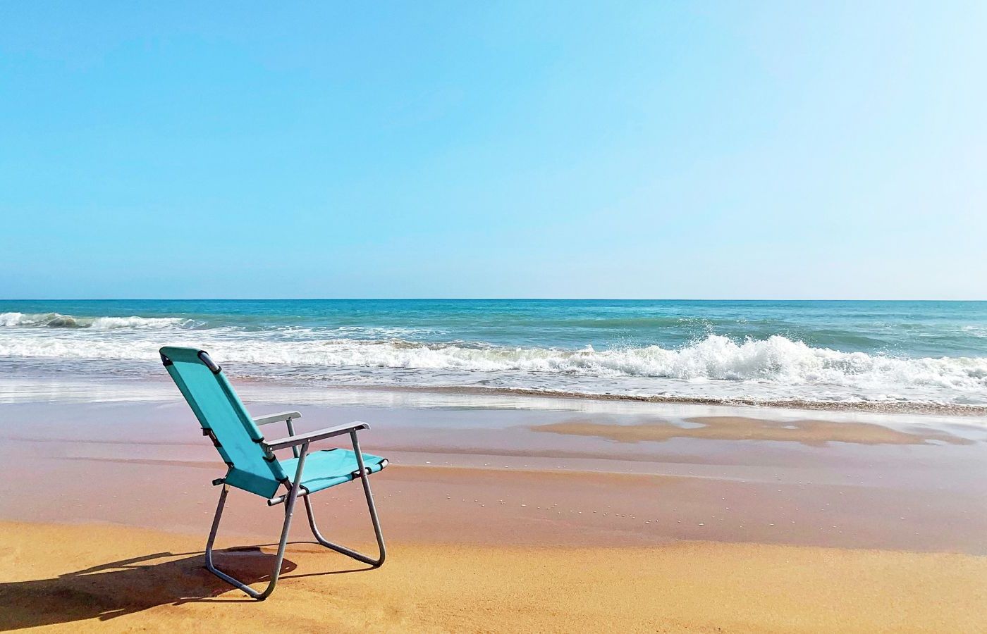 A single blue beach chair at the beach near the shoreline on a sunny day.