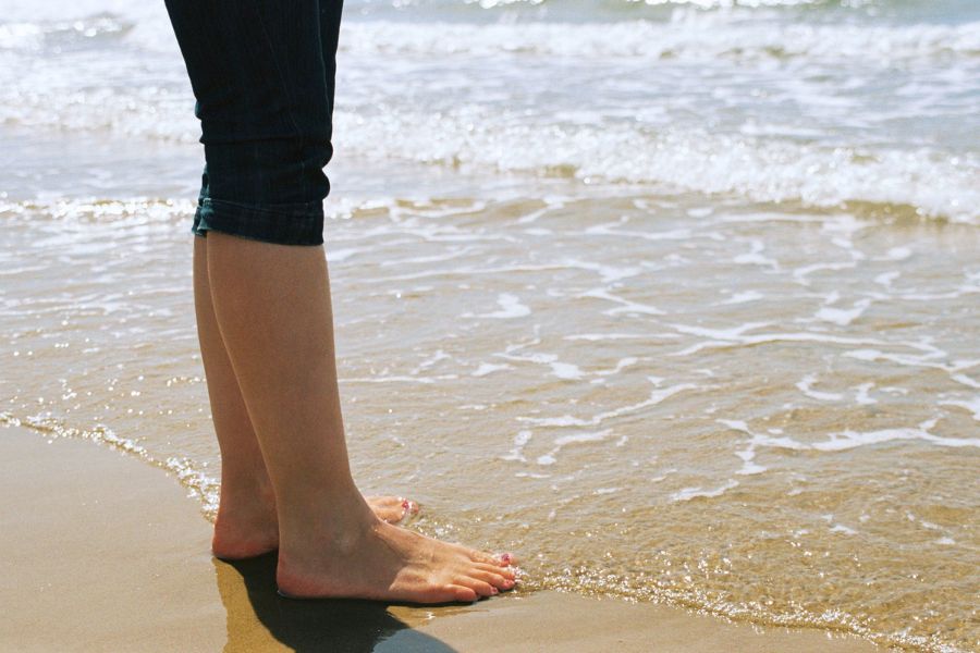 Someone shown standing barefoot at the beach from the knees down.