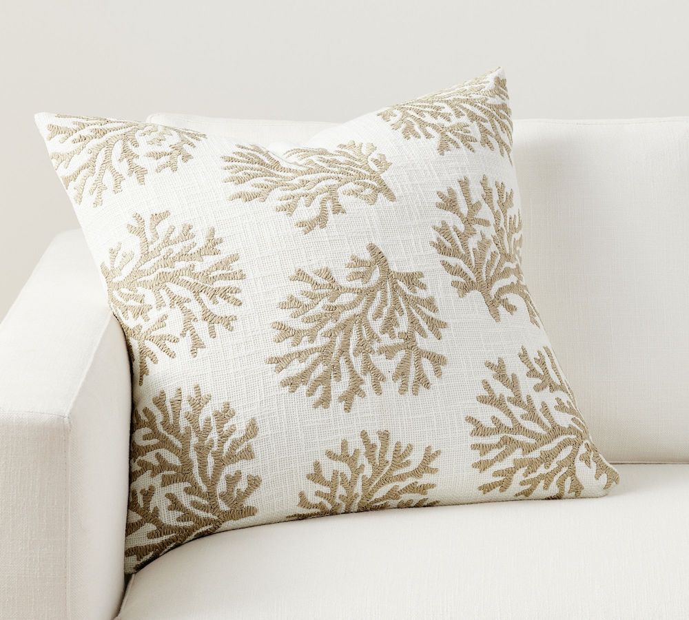 A cream colored pillow with an embroidered tan coral pattern.