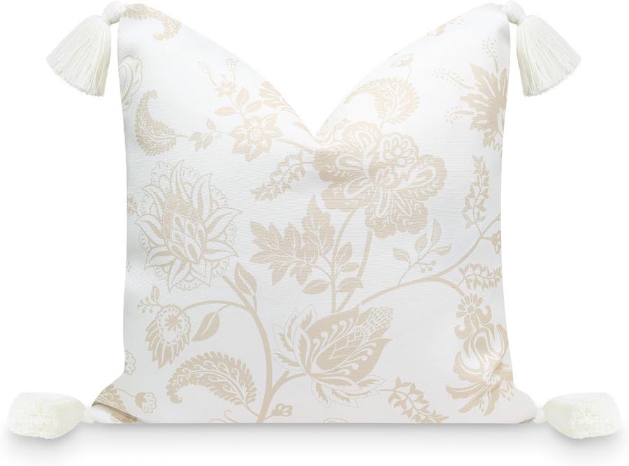 A beige and cream floral throw pillow with tassels on the corners.
