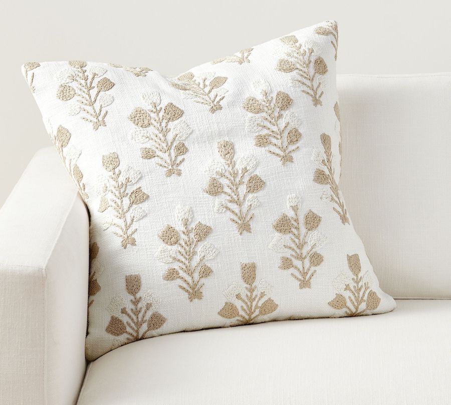 A white throw pillow with a textured beige floral pattern.