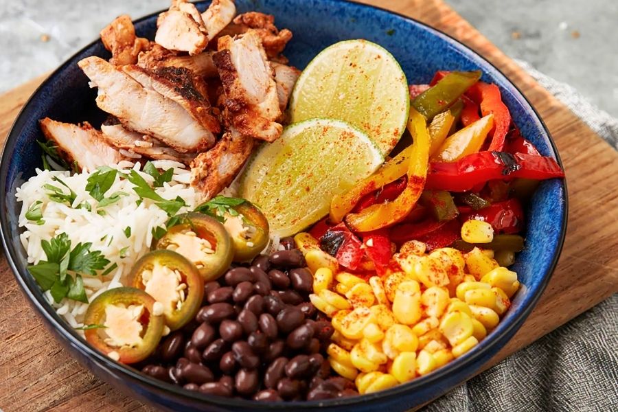 A burrito bowl with rice, chicken, jalapeno, black beans, corn, peppers, and lime.