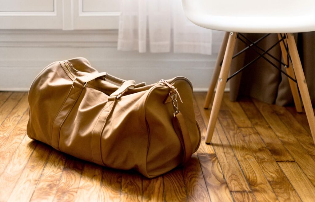 A full duffle bag on the hardwood floor of a room.