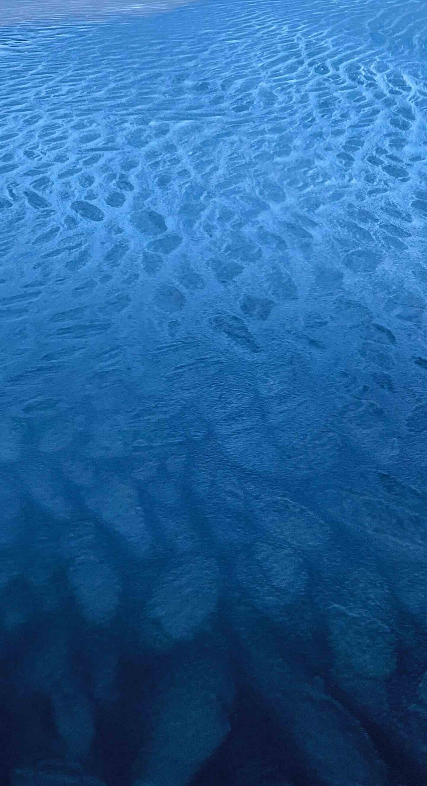 Frozen water at the beach in winter, showing patches of ice connected together on the water's surface.