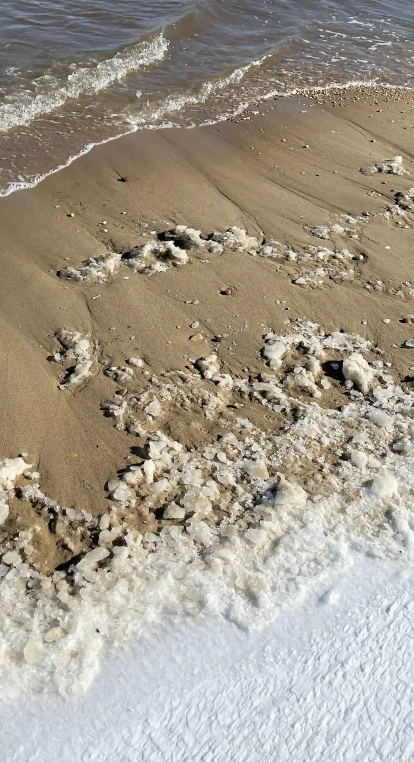 The shoreline of a beach with snow and frozen waves on the sand.
