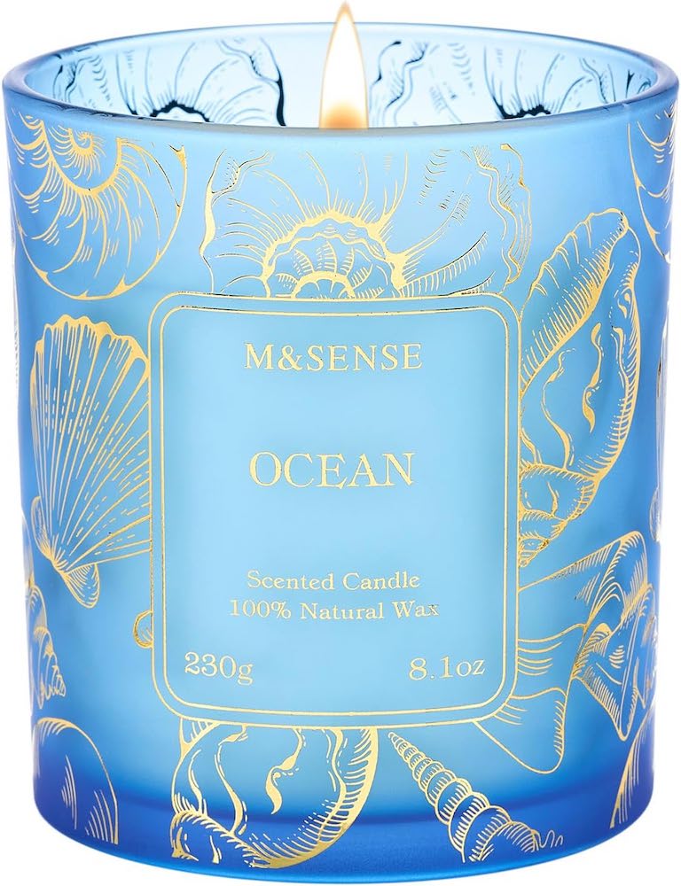 An ocean-scented candle in a blue jar with a gold shell design.