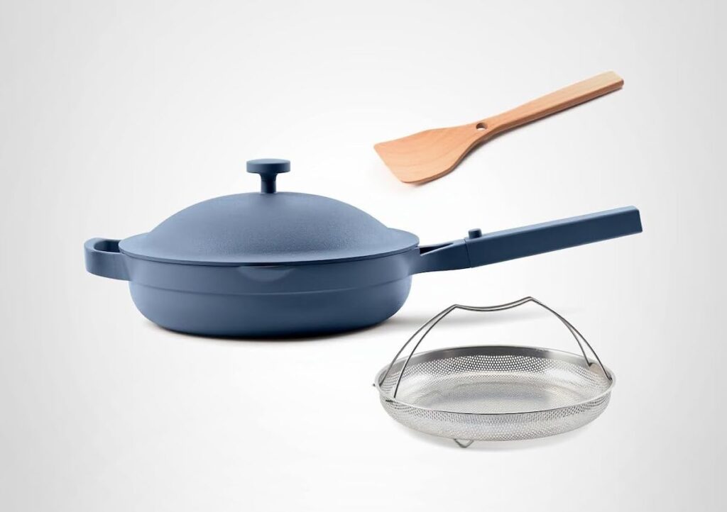 A blue nonstick pan with lid, wood spatula, and steamer basket.