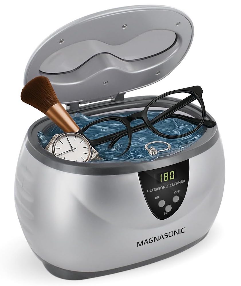 An. ultrasonic jewelry cleaner showing a watch, makeup brush, glasses, and a diamond ring in the cleaner.