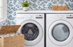 A laundry room mockup with hydrangea wallpaper, a shelf with a plant and a scalloped basket, and a woven hamper.