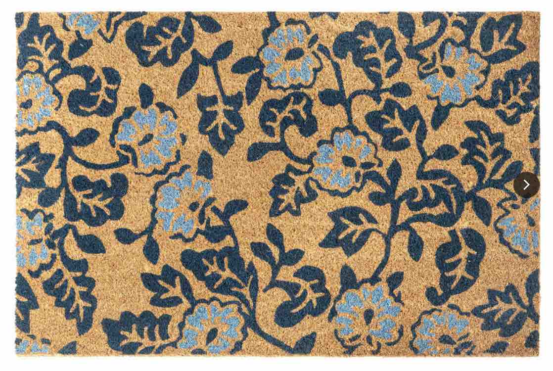 A tan door mat with a blue and navy floral pattern.