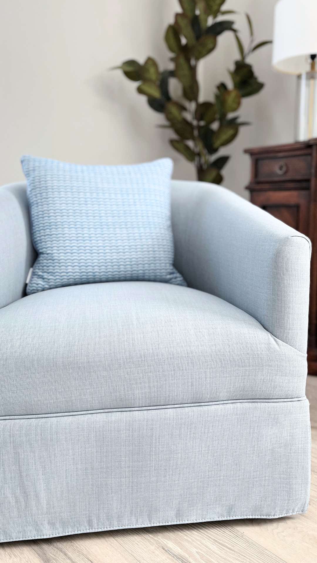 A blue skirted accent chair with an accent pillow.