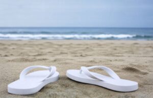 A white pair of flip flops on the beach.