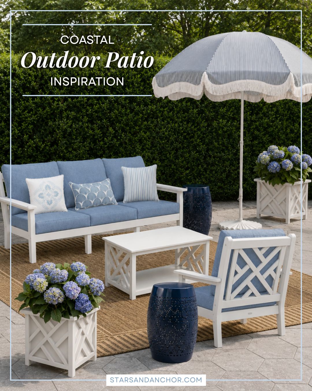 An outdoor patio featuring a blue and white couch, chair, coffee table, planters with hydrangeas, umbrella and stand, side tables, and rug on a stone patio with a hedge in the background.