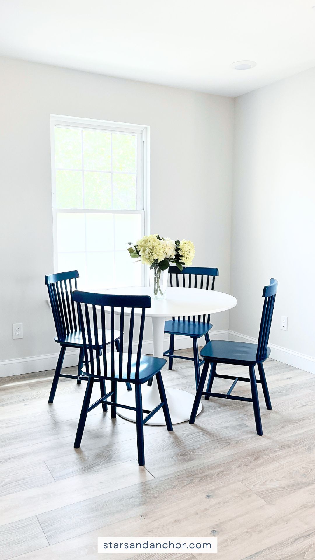A kitchen dining area with a round white table, navy blue dining chairs, and a vase with flowers.