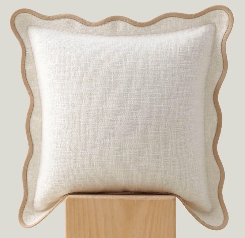 A beige throw pillow with a tan scalloped border.